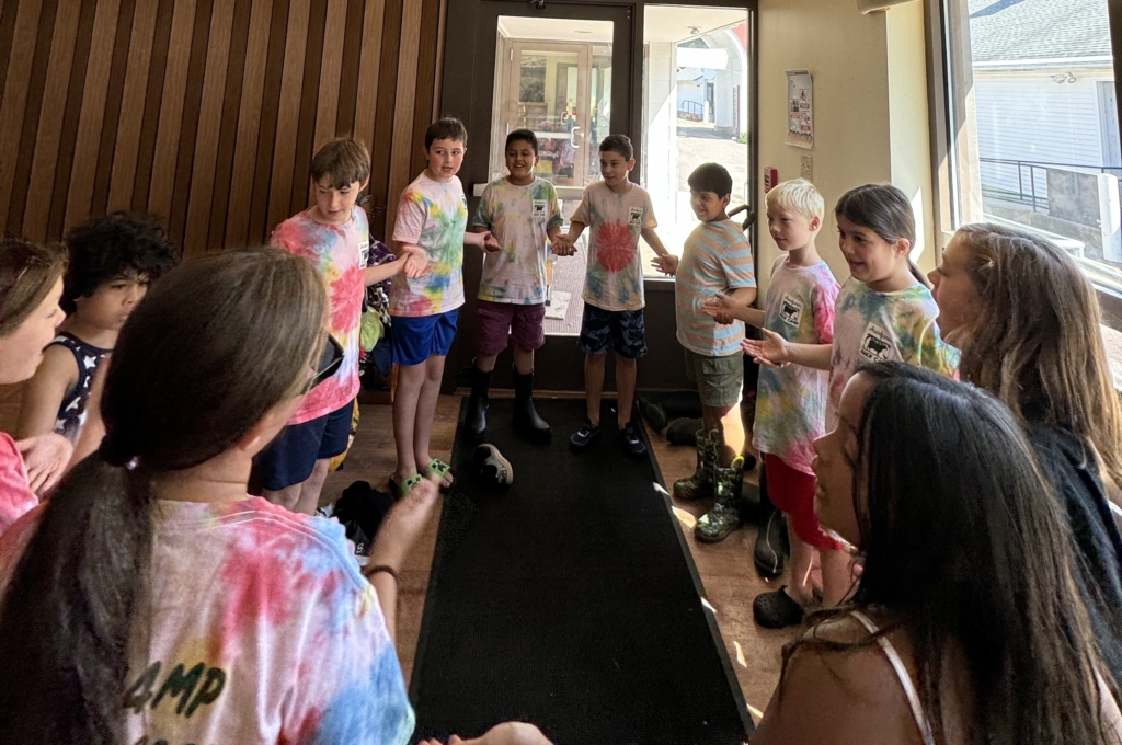 Interdistrict campers in the Daisies group join hands and play a signing game as they wait for the bus on the last day of the program.